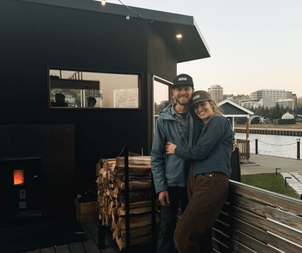 Cedar and Stone Employee's Lindsey and Neil Rasmussen stand outside in front of their social sauna outside of Pier B Resort.